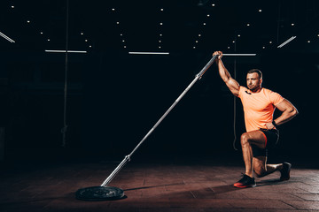 Fototapeta na wymiar handsome muscular sportsman performing lunge with bar in dark gym