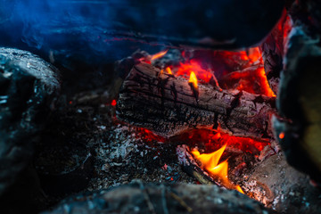 Smoldered logs burned in vivid fire. Atmospheric background with orange flame of campfire. Unimaginable detailed image of bonfire from inside with copy space. Smoke and ashes close up.