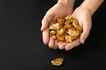 Female hands with gold nuggets on black background