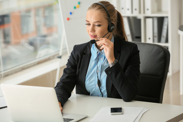 Beautiful female secretary talking through headset in office