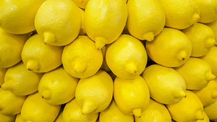 Closeup of fresh lemons in a stack at the fruit market. Yellow background