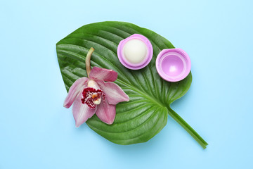 Beautiful orchid flower with leaf and hygienic lipstick on color background