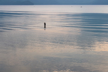 Fototapeta na wymiar Nikko, Tochigi Prefecture, Japan - July 9, 2017: A man stands fishing at Lake Chuzenji