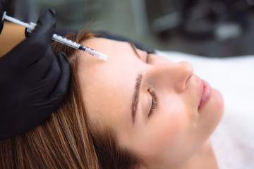 Close-up beautiful female face and cosmetologist's hands with syringe during facial beauty injections. Rejuvenation and hydratation. Cosmetology concept in clinic.