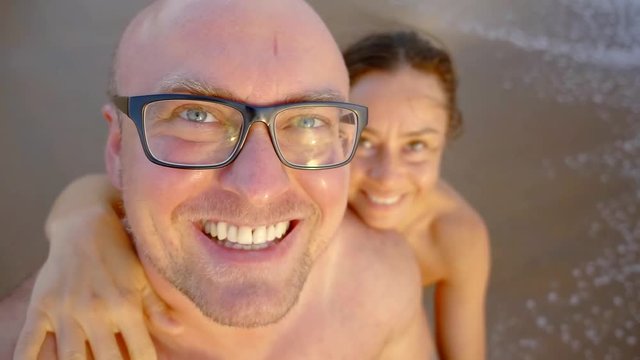 cheerful bald man and his woman are taking selfie on a camera on a wild beach near sea