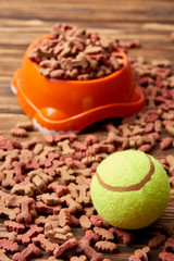 close up view of plastic bowl with dog food and ball on wooden table