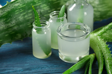 Bottles and glass with fresh aloe vera juice on color wooden table