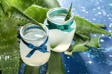 Glass jars with fresh aloe vera juice on color table