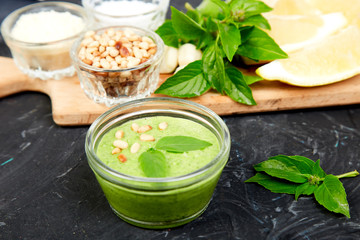 Homemade pesto sauce in glass jar with ingredients.