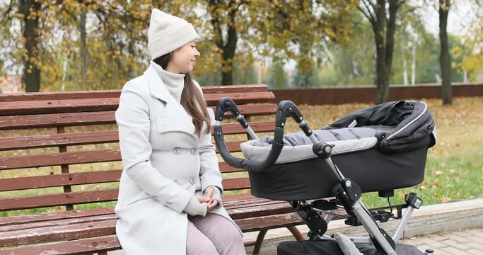 Young mother walking with her little baby son in stroller in autumn park and play with dog. Woman in coat with a stroller and a Shiba inu dog at cold weather