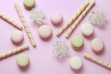 French macaroons and crispy wafer rolls on pink background.