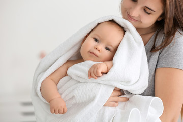 Young woman with cute little baby wrapped in soft towel at home