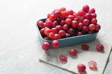 Bowl with red grapes on light background