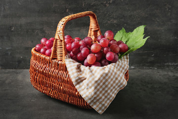Wicker basket with fresh red grapes on grey background