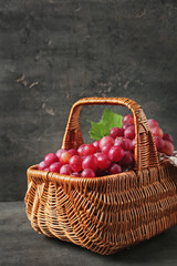 Wicker basket with fresh red grapes on grey background