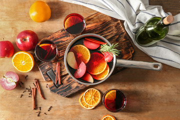 Glasses and saucepan of delicious mulled wine on wooden table