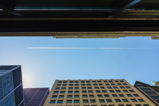 Airplane leaves trace on clear blue sky between Chicago buildings in the financial district. Chiacago, IL, USA