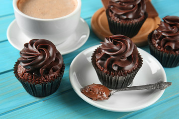 Delicious chocolate cupcakes with cup of coffee on color wooden table