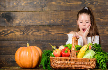 Kid farmer with harvest wooden background. Girl kid rustic style farmers market with fall harvest. Child cheerful celebrate harvest holiday pumpkin vegetables basket. Harvest festival concept