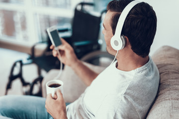 Man Listens to Music in Headphones and Holds Cup