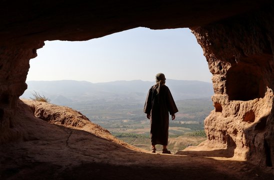 MAN WITH DJELLABA LOOKING TO THE VALLEY FROM A HIGH CAVE