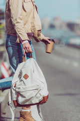 Obraz premium partial view of female traveler with backpack and coffee to go crossing road in new city
