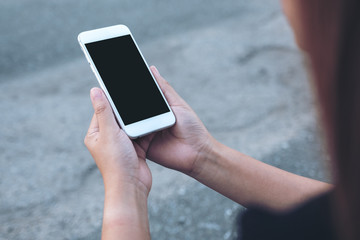 Mockup image of a woman holding white mobile phone with blank black screen with street background