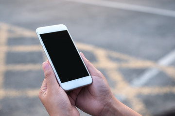 Mockup image of hand holding white mobile phone with blank black screen with street background