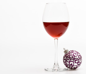 Winter celebration with alcohol drink. New year party concept. Wineglass with red liquid or wine and christmas ball ornament isolated on white background. Glass with wine and christmas decoration