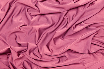 Background and texture. The concept of a hobby and production. Image of the texture of the fabric for sewing clothes. Pink knitwear, silk. Abstraction. Cropped shot, isolated, close-up, blurred, horiz