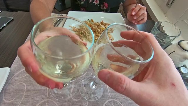 SLOW MOTION: two white wine glasses doing cheers with hands and celebrate in a restaurant, set table background and slow motion effect.