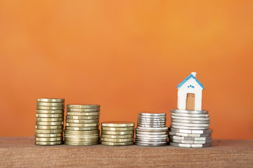Gold and silver coins with miniature house over blurred orange background, business and finance concept, investment and property business