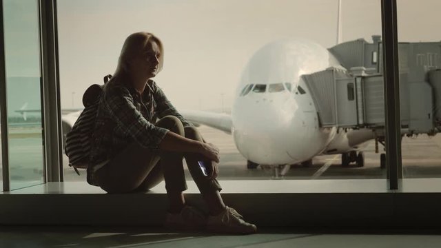 A single woman is sitting on the windowsill in the airport terminal amid a huge airliner. Loneliness and parting concept