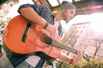 Let music flow. Low angle of reflective male guitarist performing with guitar and strumming strings on street