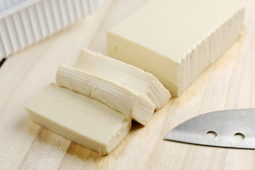 Tofu is cut into pieces placed on a chopping board.
