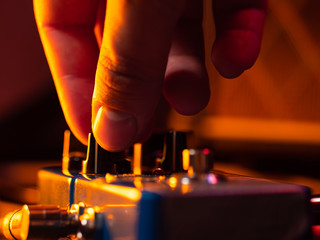 Musician tuning guitar effect pedal for best music during concert on stage. Guitarist tapping on it...