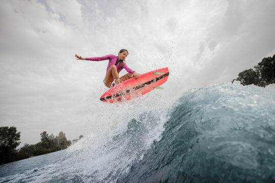 Active and young woman wakesurfer jumping up the blue splashing wave against sky