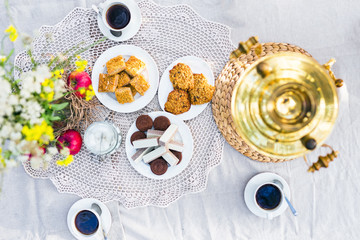 Table with samovar, coffee and sweets decorated with flowers outdoors