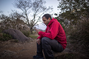 Obraz premium Man in red jacket using phone in left hand beside dirt trail in nature