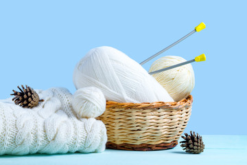 White threads for knitting, knitting needles and a white knitted sweater on a blue background. Knitting concept. Knitted and winter clothes