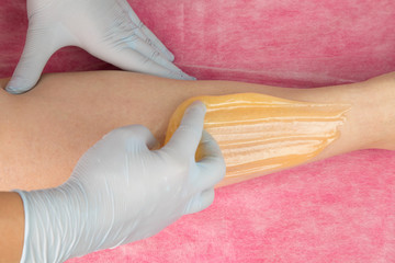 Removing unnecessary hair on the legs. Procedure sugaring in a beauty salon.Depilatory sugar paste