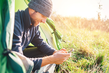 Man traveler portrait using his mobile phone and sitting in camping tent in wild nature
