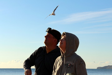 Father and son feeding seagulls on the sea coast