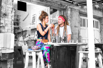 Clanging glasses. Couple of flower children wearing bright clothes clanging their glasses with...