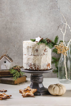 Autumn homemade white naked cake decorated by rated by star cookie and green thuja branches on cake stand fir tree, cookies, xmas decor above on white marble table. grey wall at background.