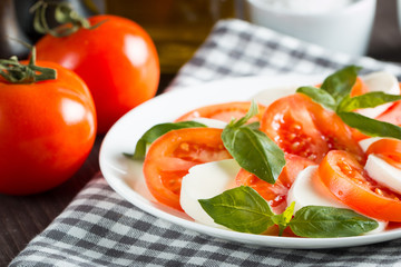 Photo of Caprese Salad with tomatoes, basil, mozzarella, olives and olive oil on wooden background. Italian traditional caprese salad ingredients. Mediterranean, organic and natural food concept.