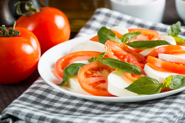 Photo of Caprese Salad with tomatoes, basil, mozzarella, olives and olive oil on wooden background. Italian traditional caprese salad ingredients. Mediterranean, organic and natural food concept.