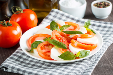 Photo of Caprese Salad with tomatoes, basil, mozzarella, olives and olive oil on wooden background. Italian traditional caprese salad ingredients. Mediterranean, organic and natural food concept.