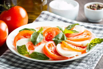 Photo of Caprese Salad with tomatoes, basil, mozzarella, olives and olive oil on wooden background. Italian traditional caprese salad ingredients. Mediterranean, organic and natural food concept.