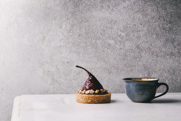 Sweet red wine tartlet with cup of coffee espresso standing on white marble table with grey wall at background. Minimalist style. Copy space